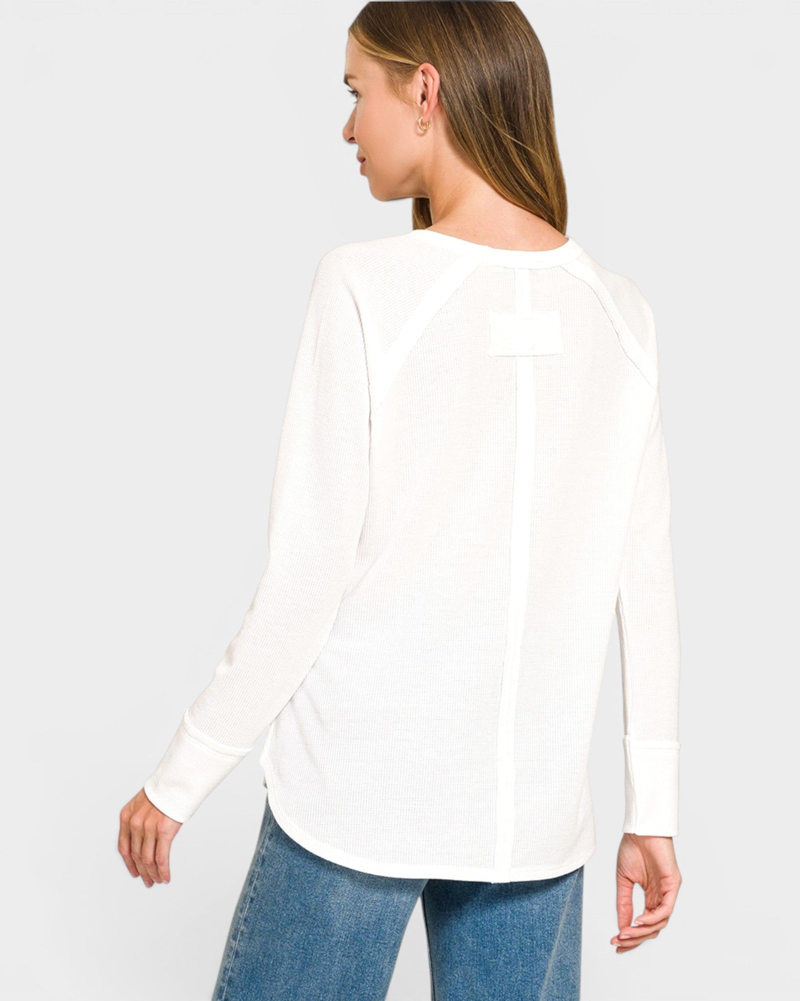 Woman wearing a white long-sleeve top and blue jeans on a light gray background