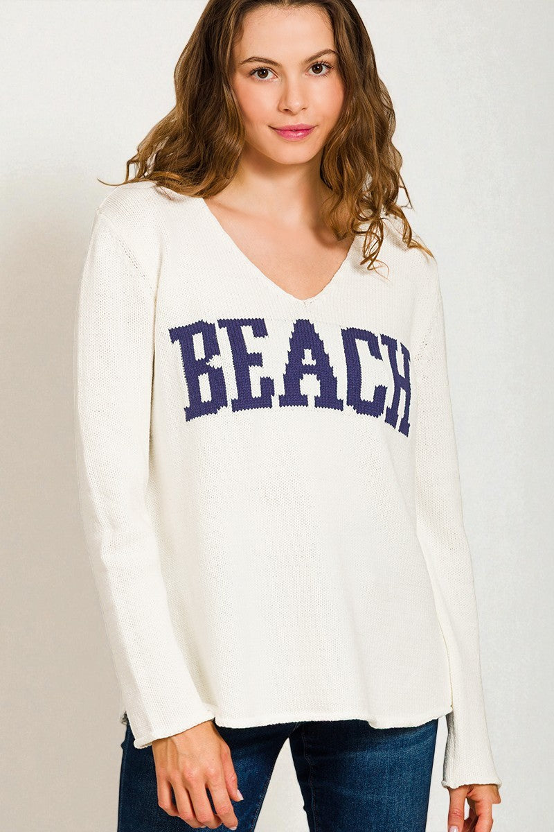 Woman wearing a white sweatshirt with 'BEACH' printed in blue on a plain background