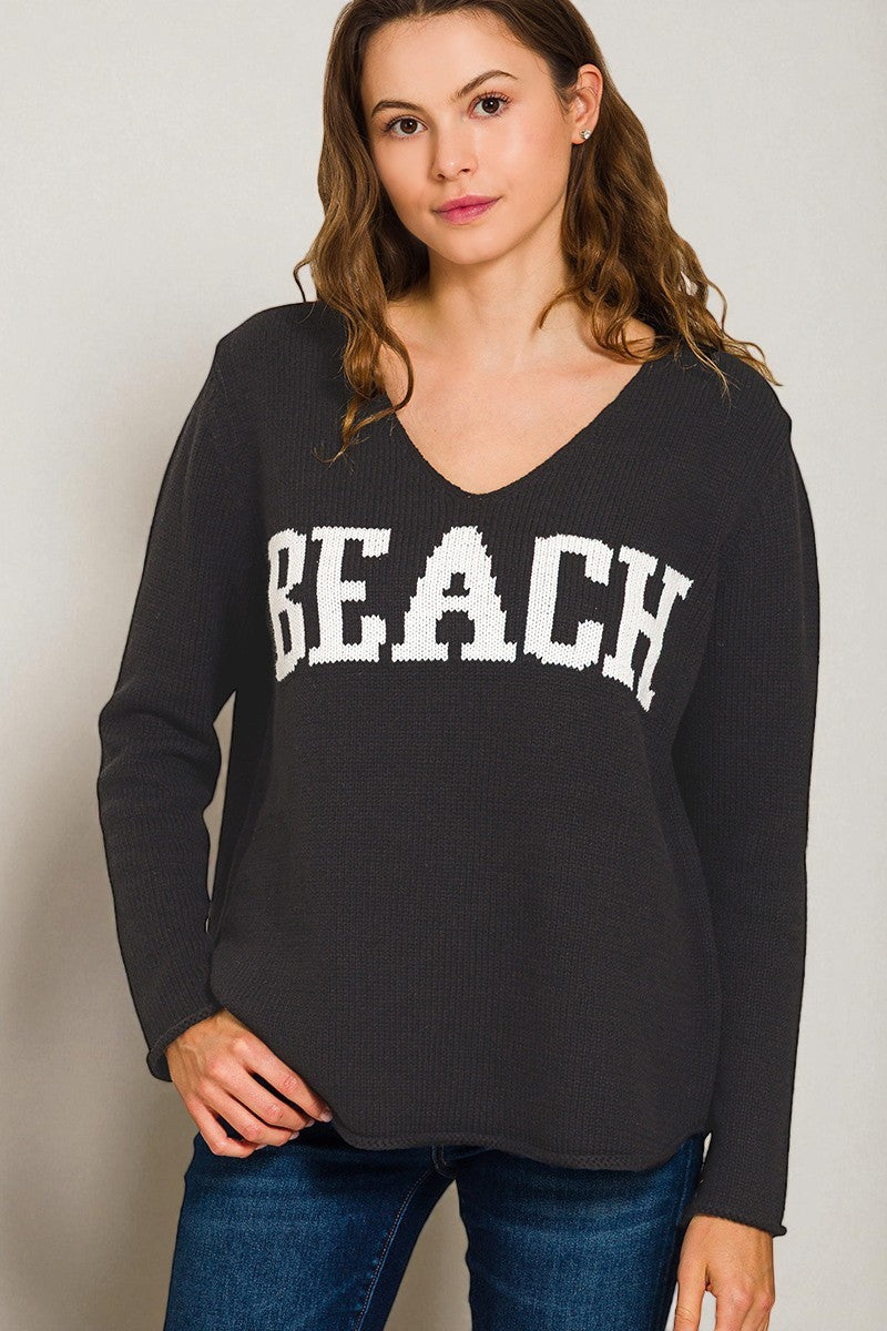 Woman wearing a black sweatshirt with 'BEACH' printed on it against a plain background