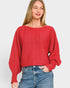 Woman wearing a red sweater and blue jeans on a plain background