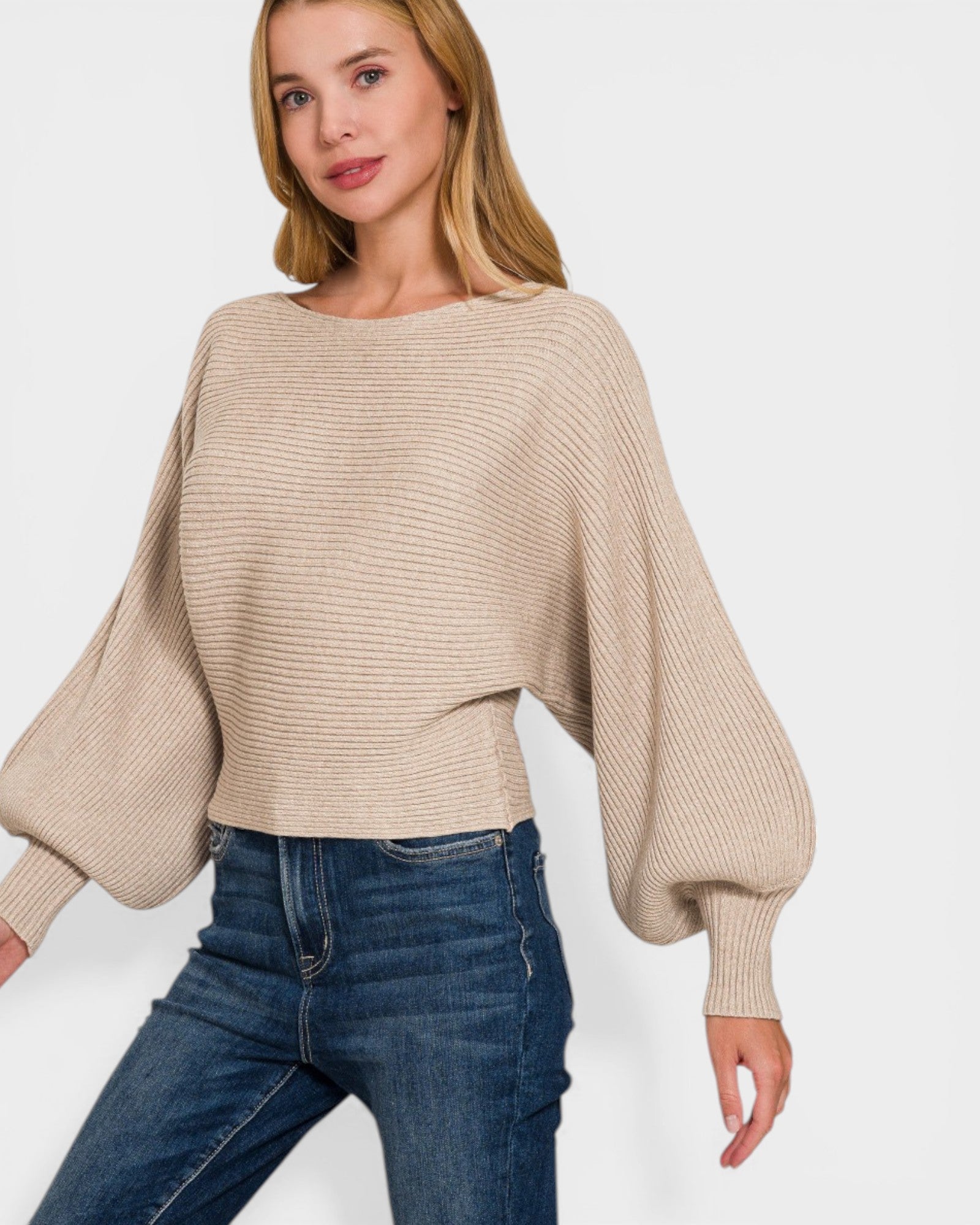 Woman wearing a beige ribbed sweater and blue jeans on a white background