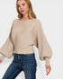 Woman wearing a beige ribbed sweater and blue jeans on a white background