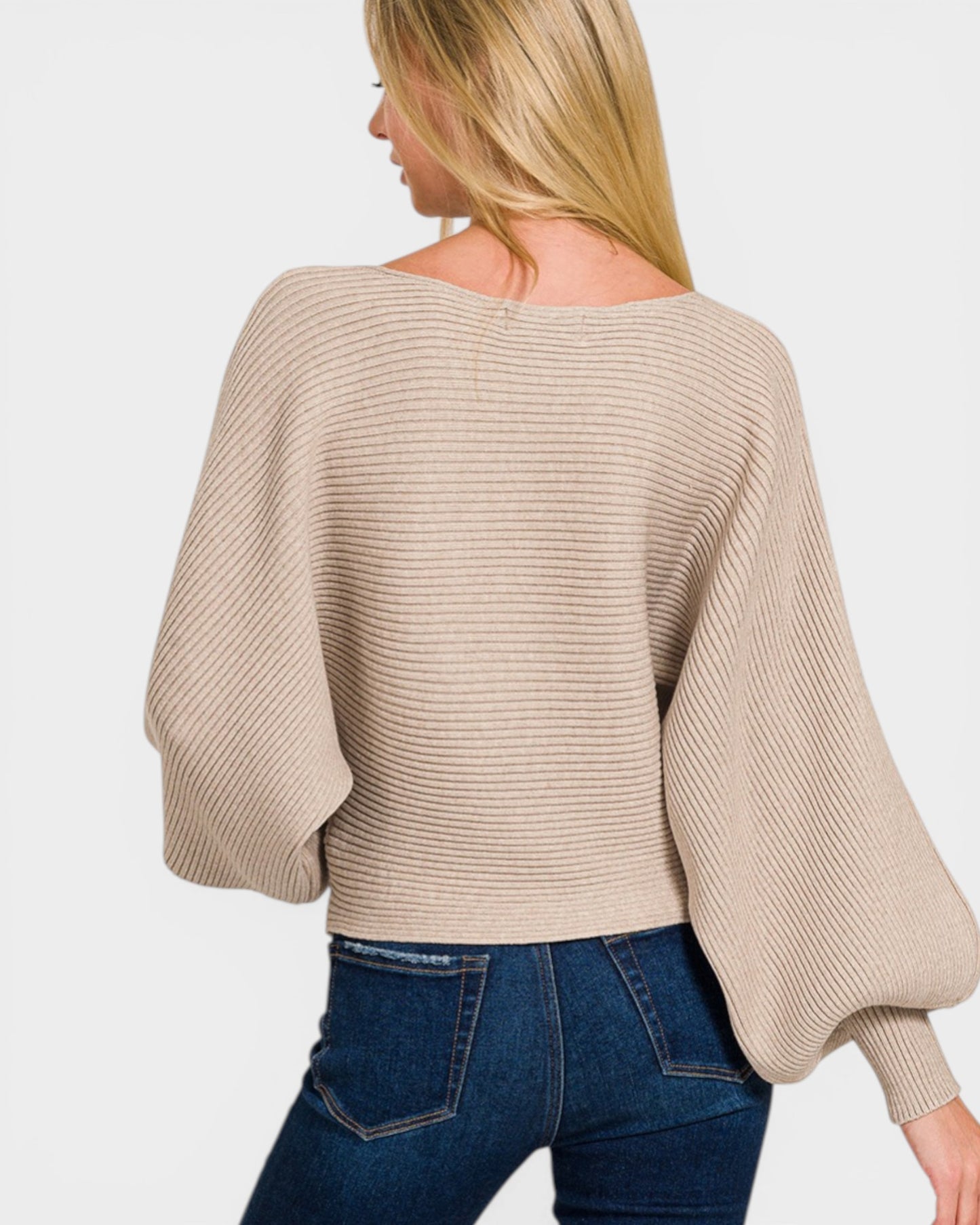 Woman wearing a beige sweater and blue jeans on a white background