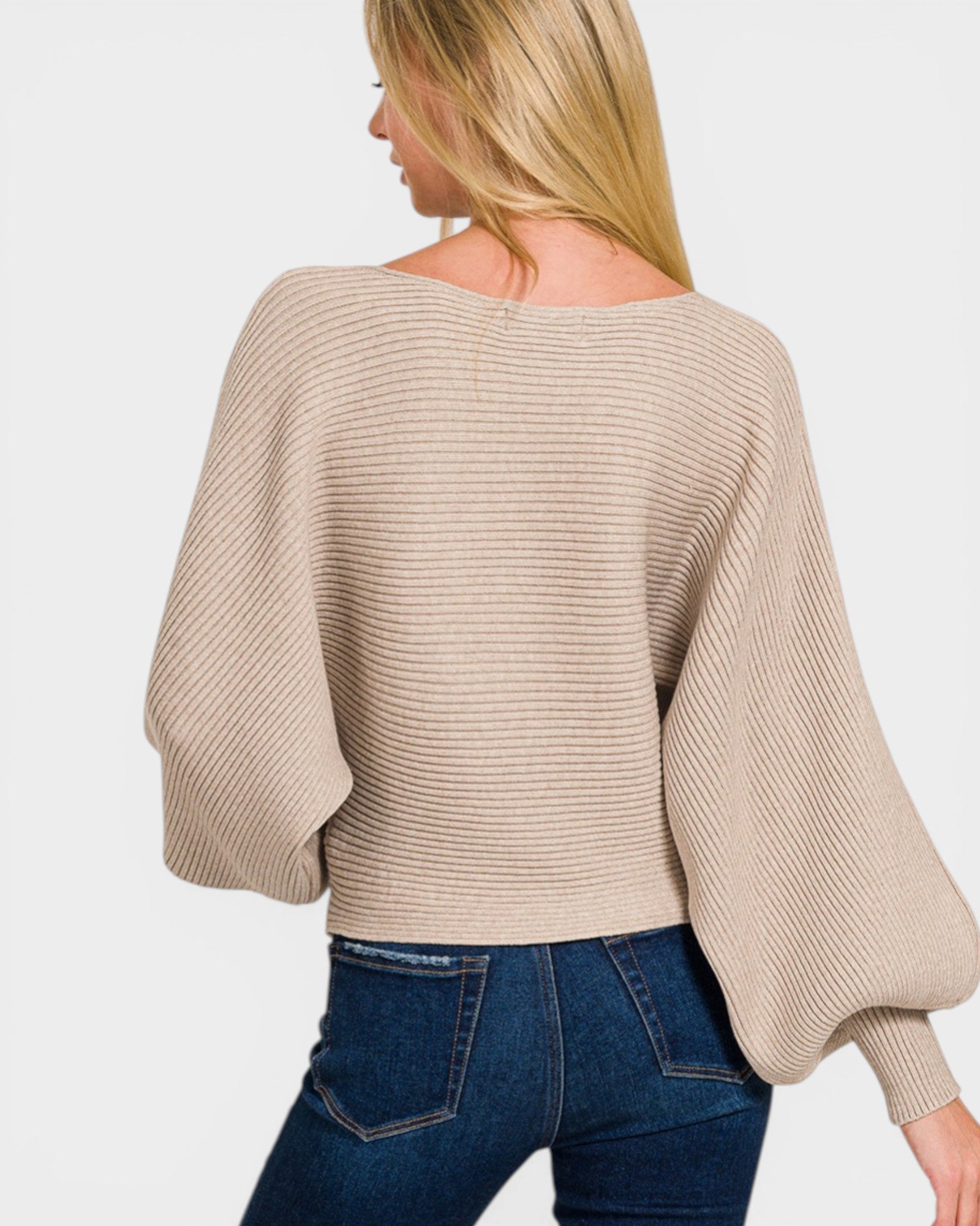 Woman wearing a beige sweater and blue jeans on a white background