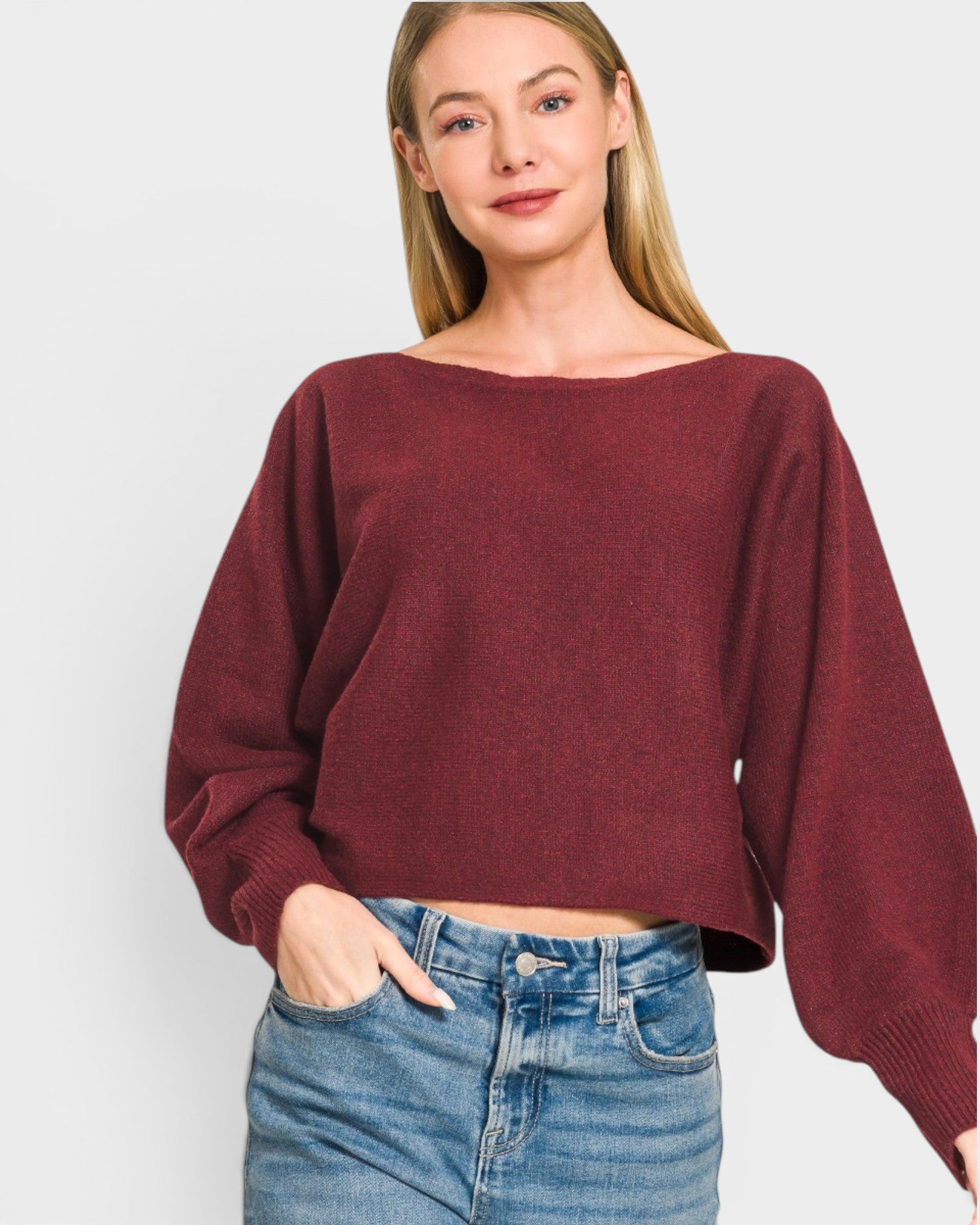 Woman wearing a burgundy sweater and blue jeans on a white background