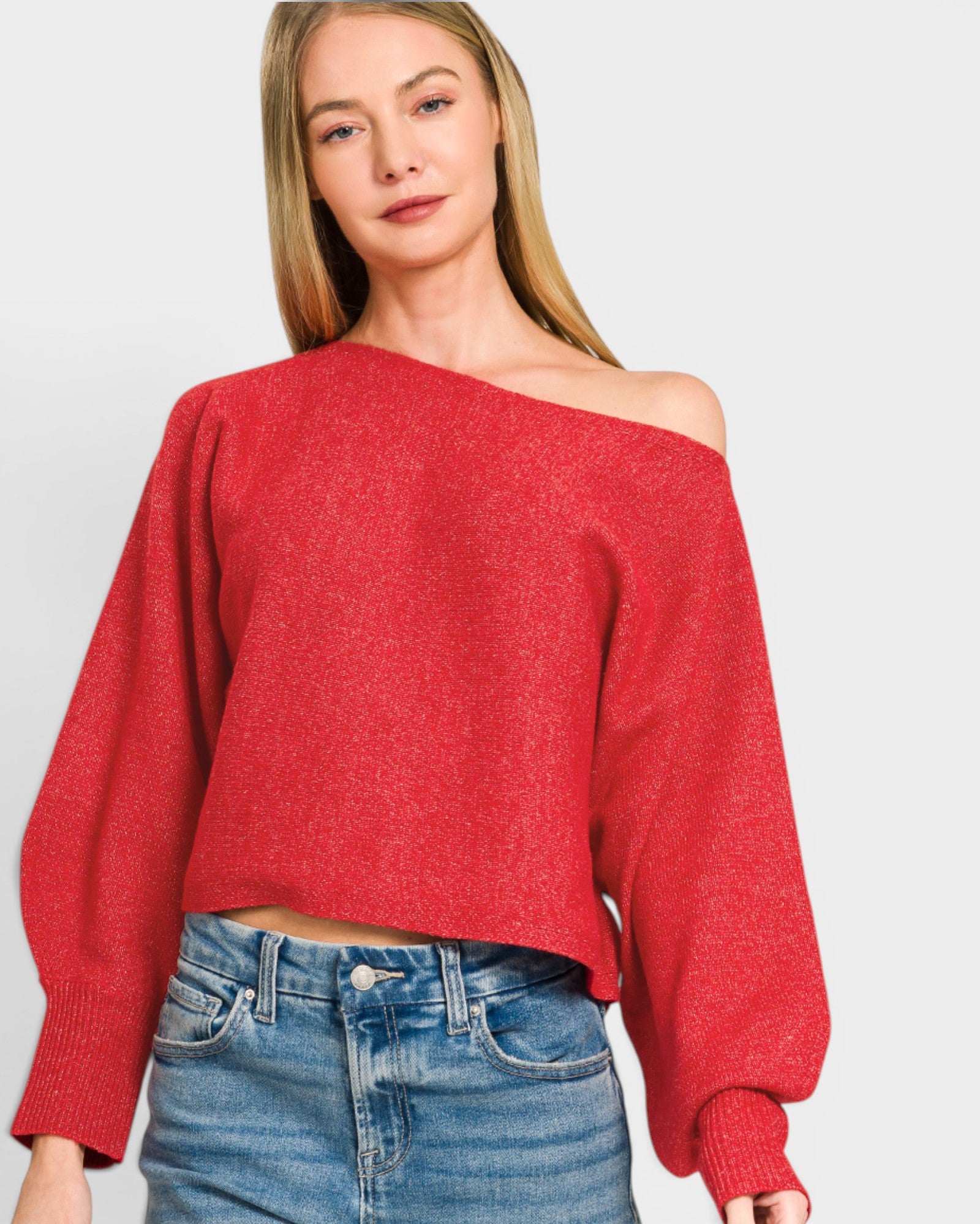 Woman wearing a red off-shoulder sweater and blue jeans on a light gray background
