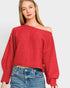 Woman wearing a red off-shoulder sweater and blue jeans on a light gray background