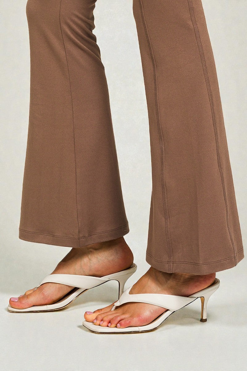 White high-heeled sandals worn with brown pants on a light background