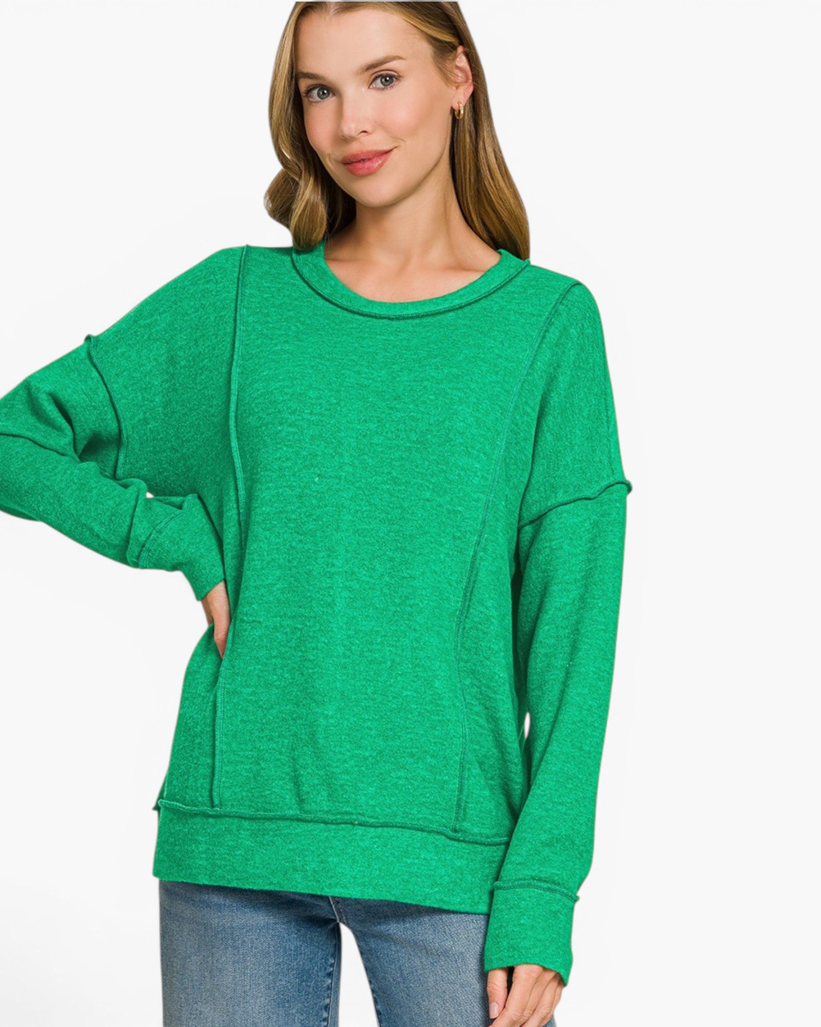 A woman wearing a bright green heathered long-sleeve sweatshirt with a relaxed, oversized fit and side pockets, paired with blue jeans, against a plain white background.
