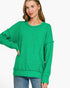 A woman wearing a bright green heathered long-sleeve sweatshirt with a relaxed, oversized fit and side pockets, paired with blue jeans, against a plain white background.