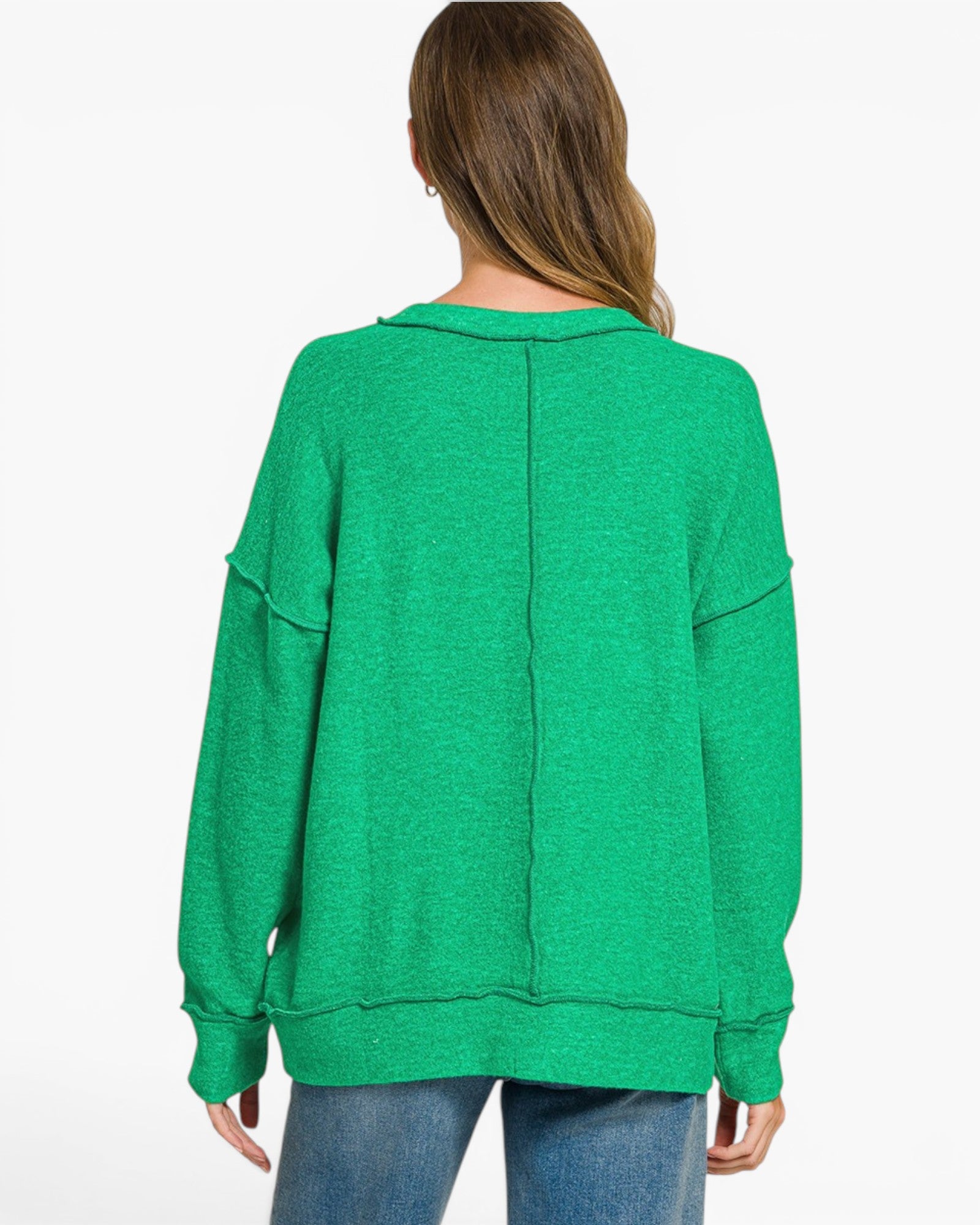A woman viewed from the back wearing a bright green oversized knit sweater with long sleeves and a relaxed fit, paired with blue jeans against a plain white studio background.