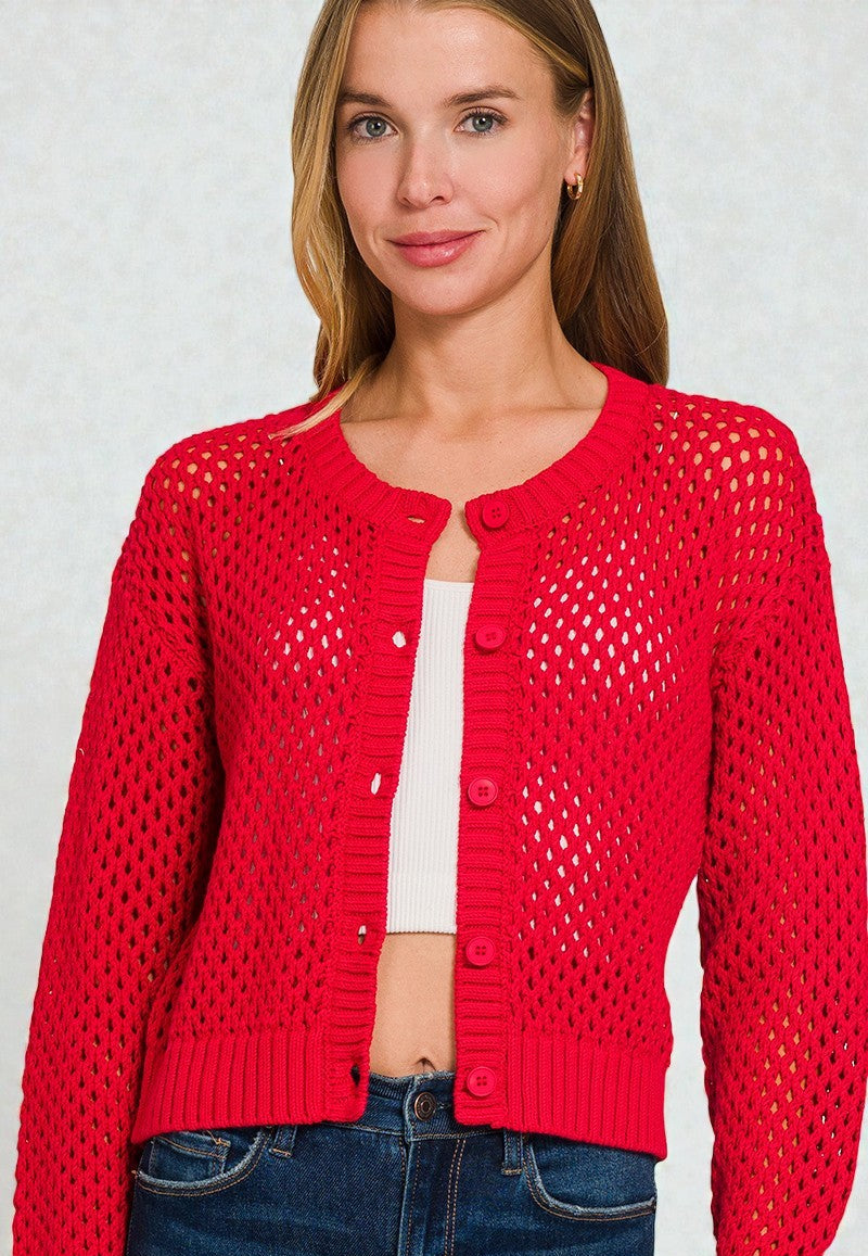 Woman wearing a red open-knit cardigan over a white top and blue jeans on a light gray background.