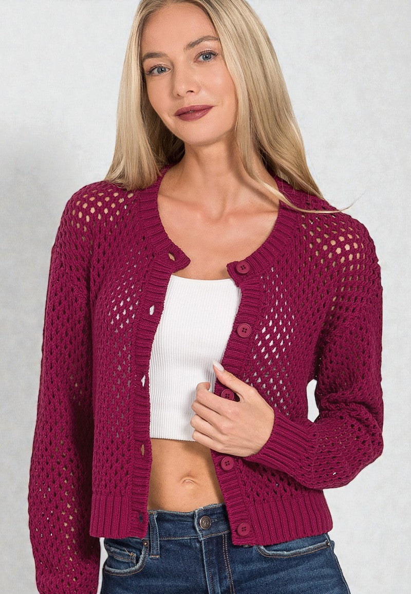 Woman wearing a burgundy knitted cardigan over a white top and blue jeans on a plain background