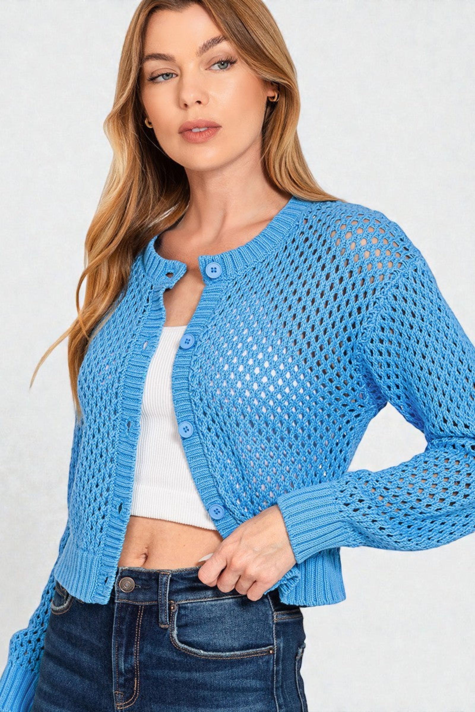 Woman wearing a blue knitted cardigan over a white top and jeans on a light gray background