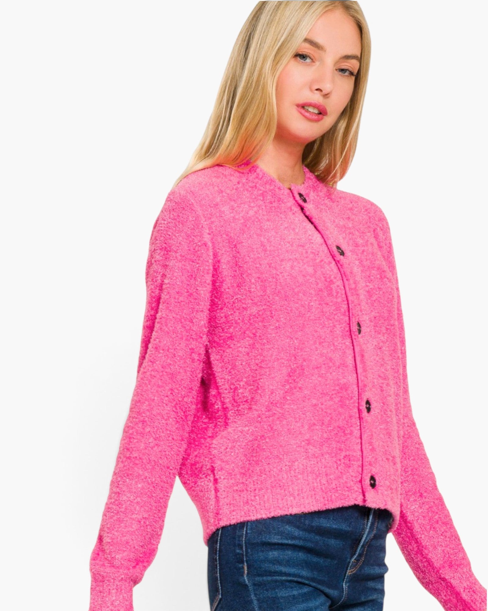 A woman wearing a bright pink fuzzy long-sleeve cardigan with dark buttons, paired with blue jeans, against a plain white background.