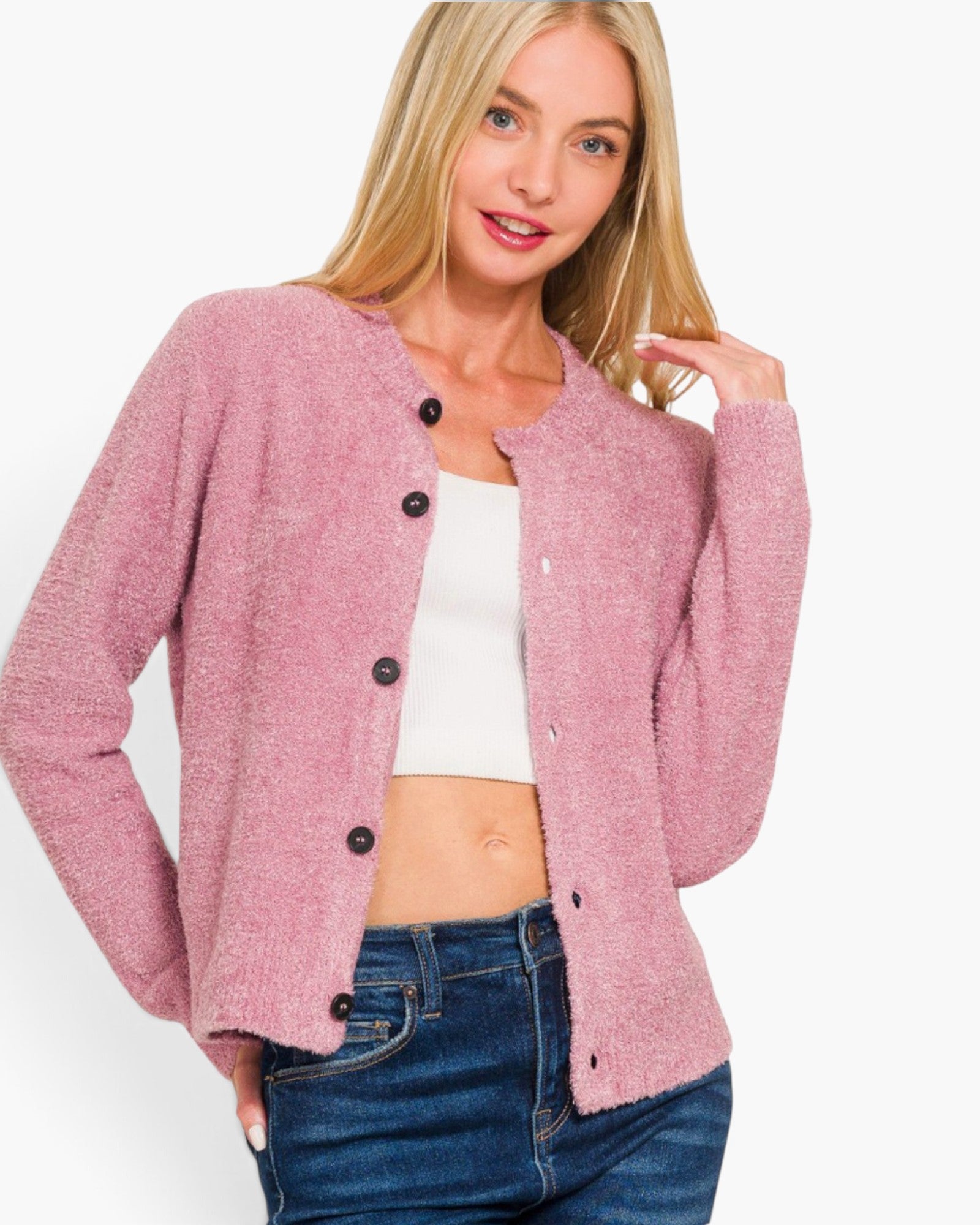 A woman wearing a pink textured button-front cardigan over a white crop top and blue jeans, photographed against a plain light background.