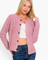 A woman wearing a pink textured button-front cardigan over a white crop top and blue jeans, photographed against a plain light background.