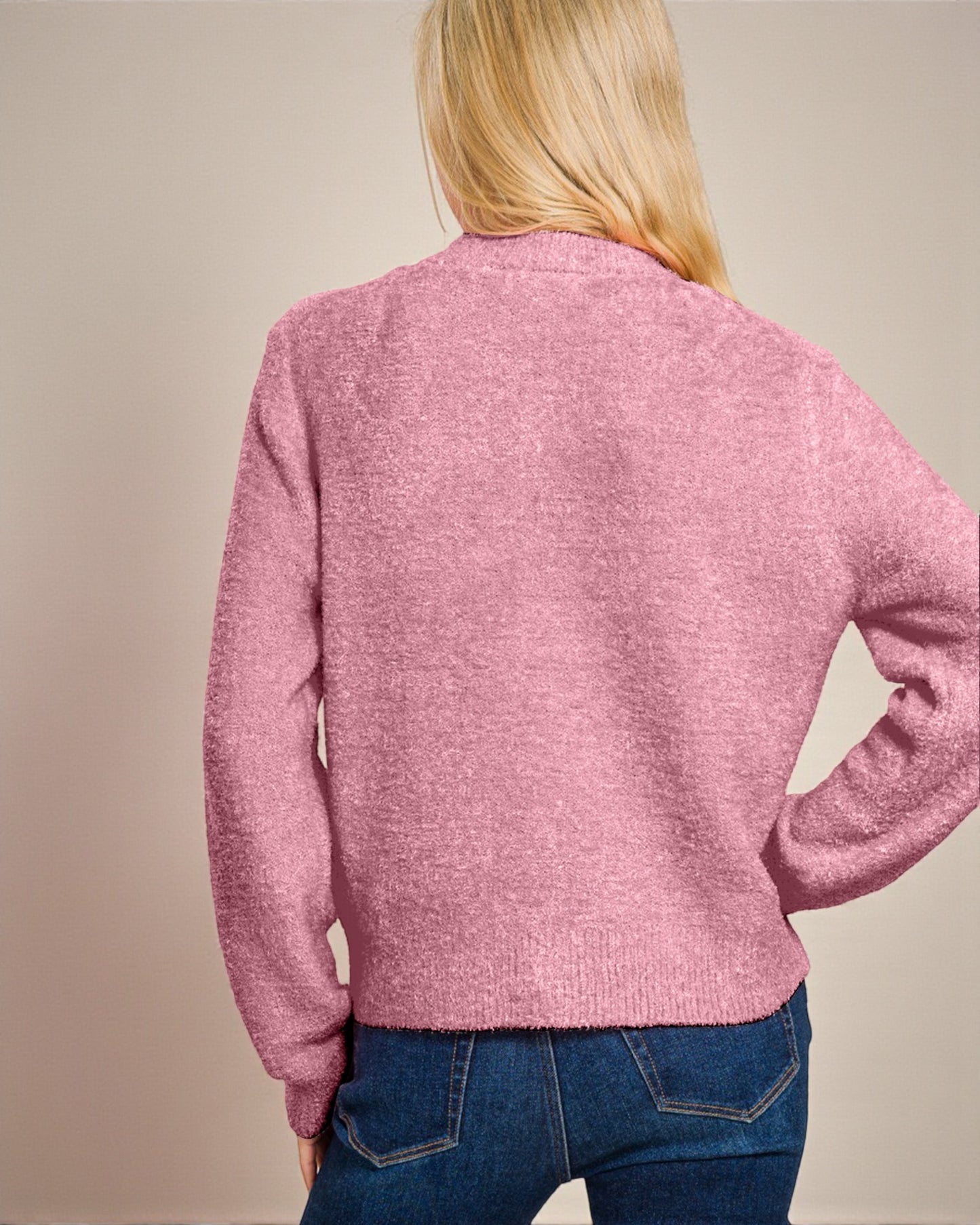 Person wearing a pink sweater and blue jeans against a beige background