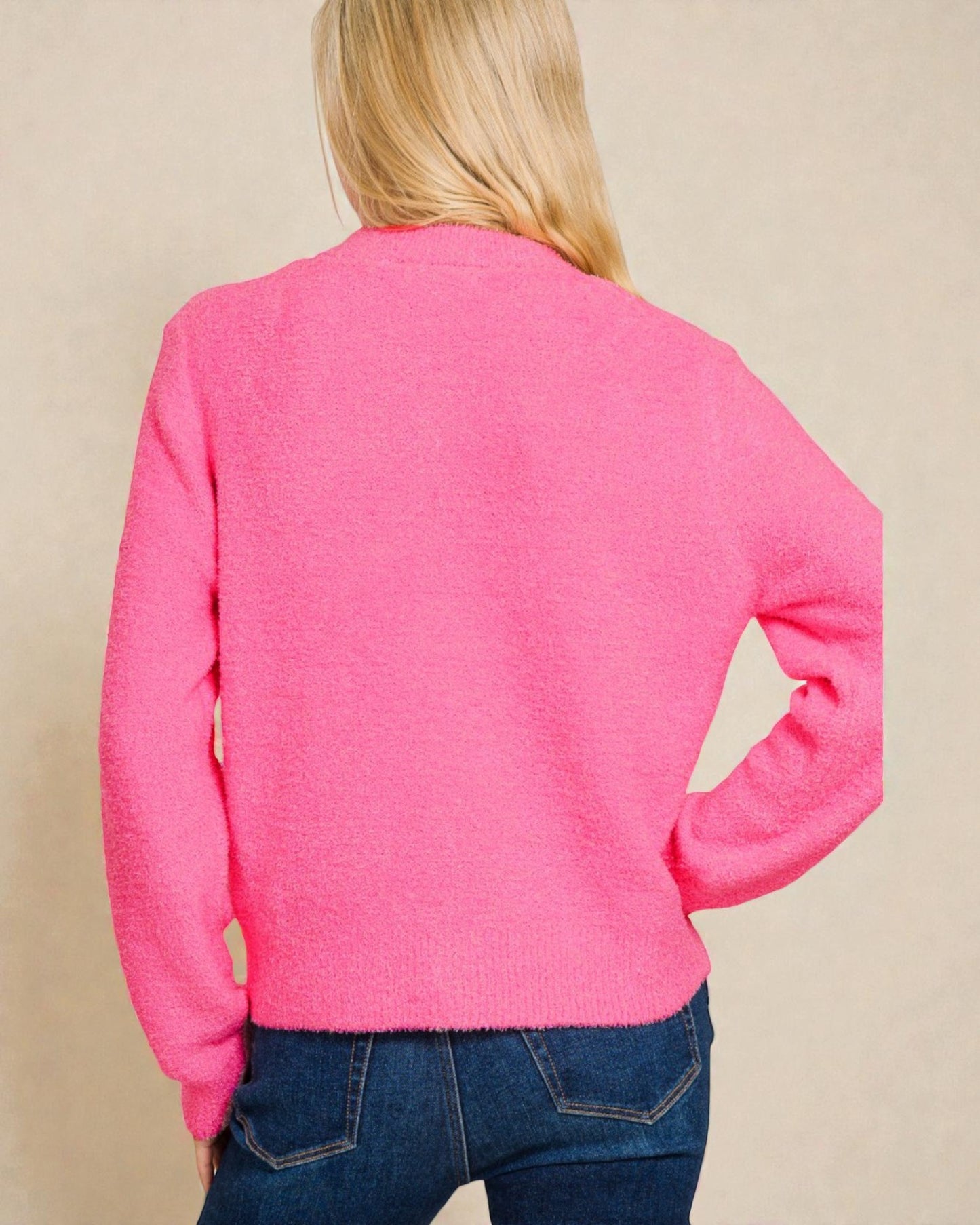 Person wearing a bright pink sweater and blue jeans on a beige background