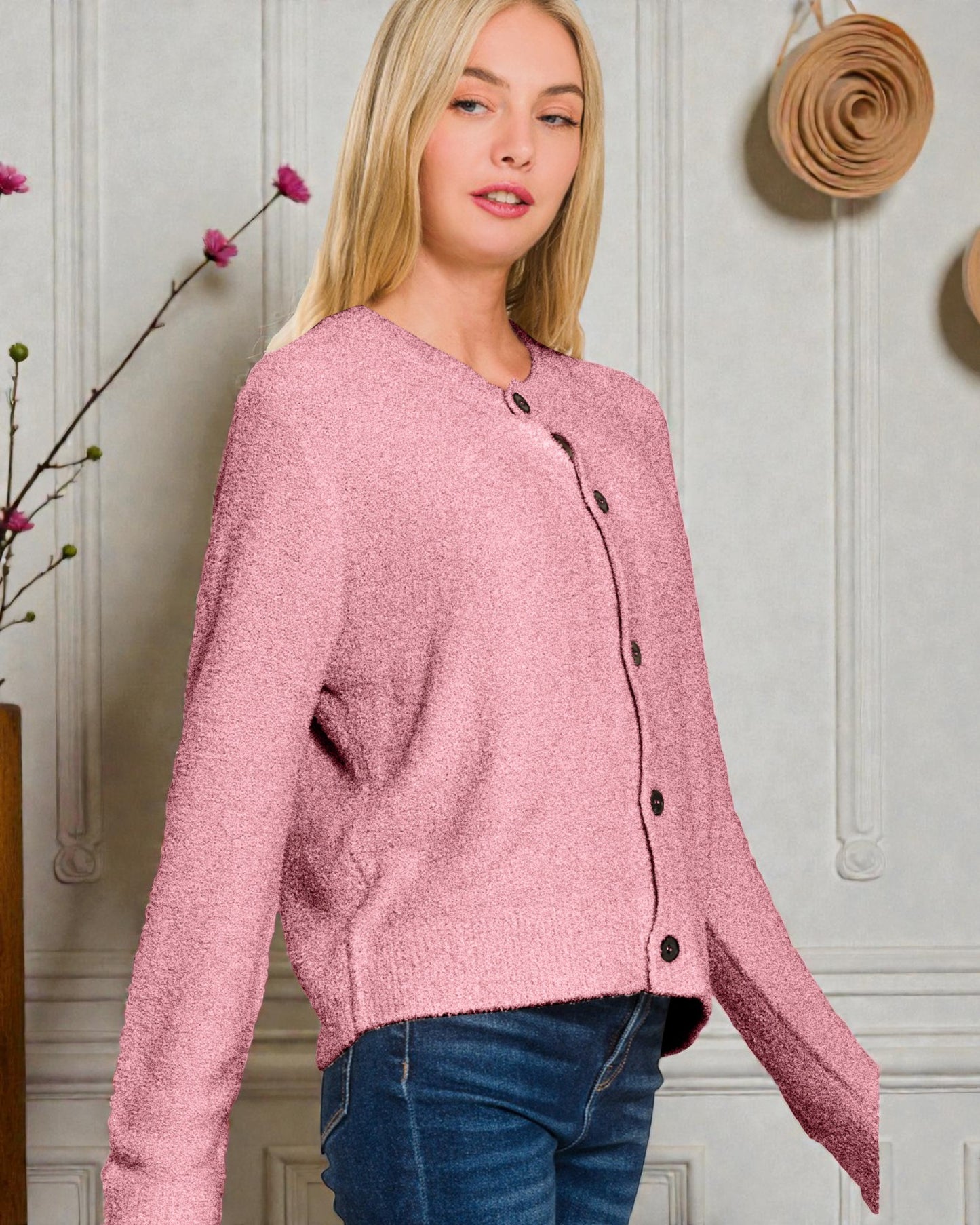 Woman wearing a pink cardigan with black buttons against a light-colored wall.