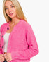 A blonde woman wearing a bright pink fuzzy knit cardigan with dark buttons over a white top, photographed against a clean white background.