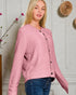 Woman wearing a pink cardigan with black buttons against a light-colored wall.