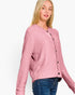 A woman wearing a textured, fuzzy pink button-up cardigan sweater and blue jeans, photographed against a clean white studio background.