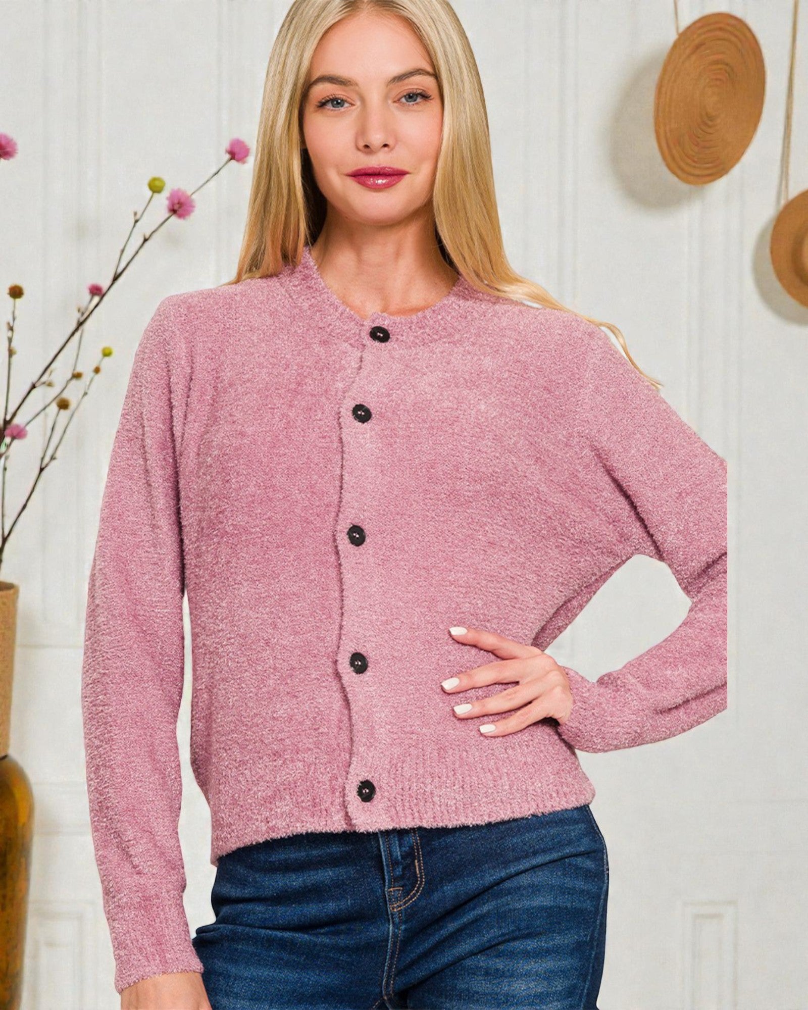 Woman wearing a pink cardigan with black buttons against a white wall.
