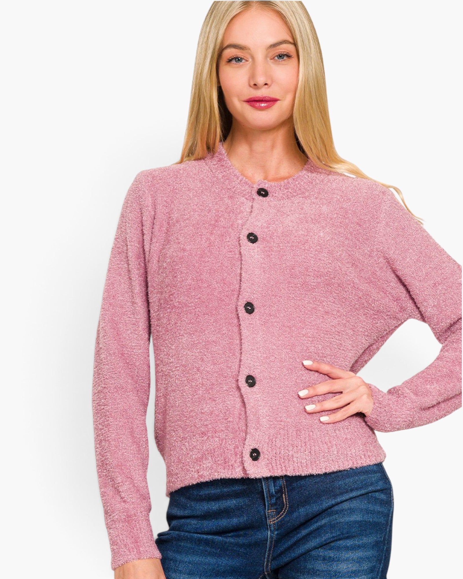 A woman wearing a dusty pink knit cardigan with black buttons and blue jeans, photographed against a plain white studio background.