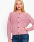 A woman wearing a dusty pink knit cardigan with black buttons and blue jeans, photographed against a plain white studio background.