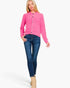 A woman modeling a bright pink knit cardigan with a stand collar and button front, paired with dark blue skinny jeans and beige ankle boots, against a plain white studio background.