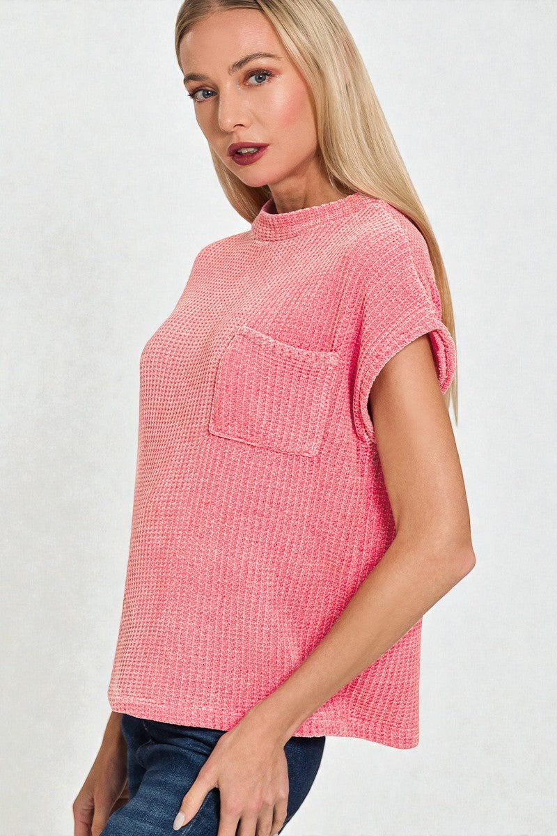 Woman wearing a pink textured top with a pocket on a white background