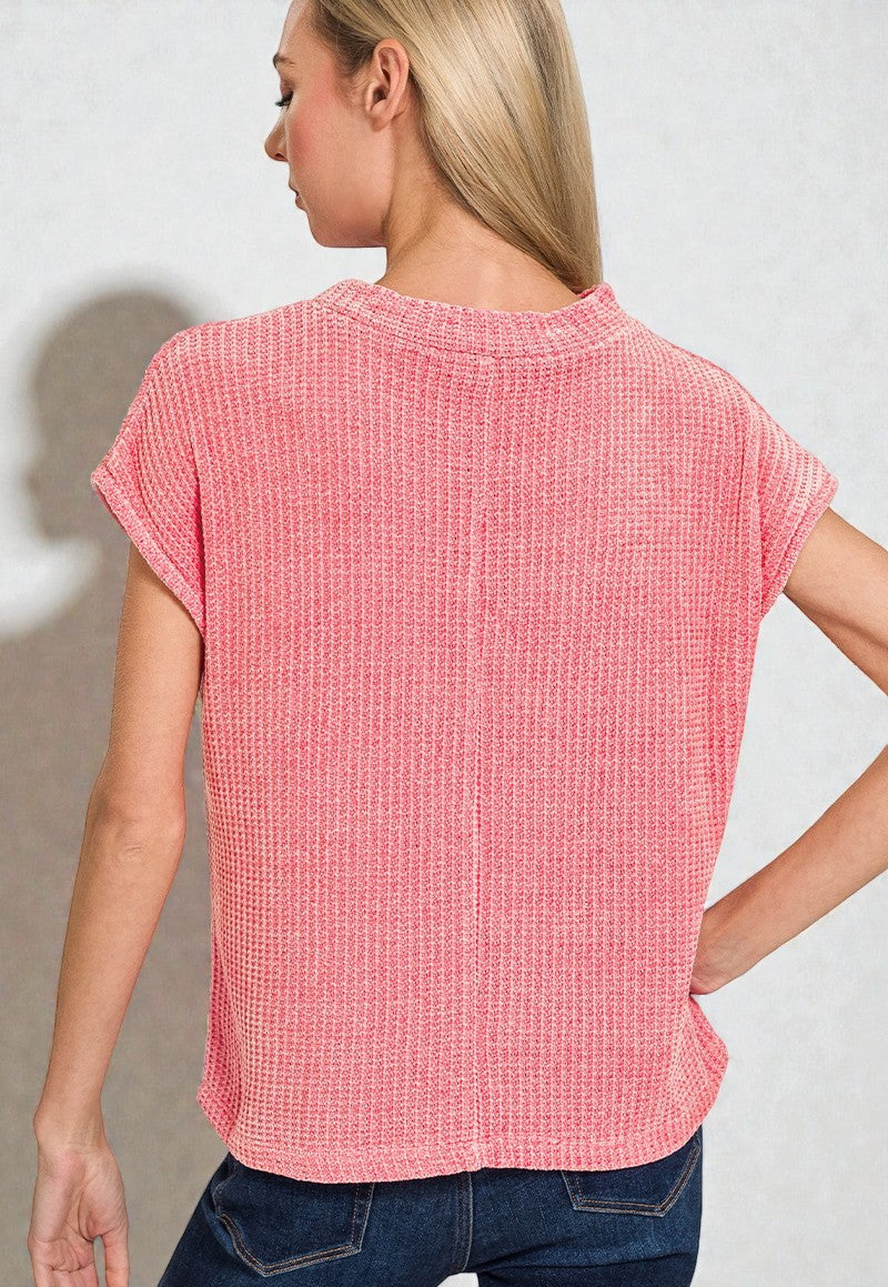 Woman wearing a pink textured top and blue jeans against a plain background