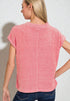 Woman wearing a pink textured top and blue jeans against a plain background