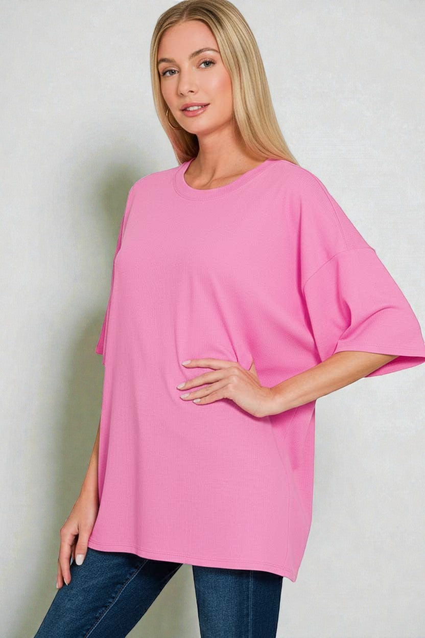 Woman wearing a pink oversized top and blue jeans against a plain background