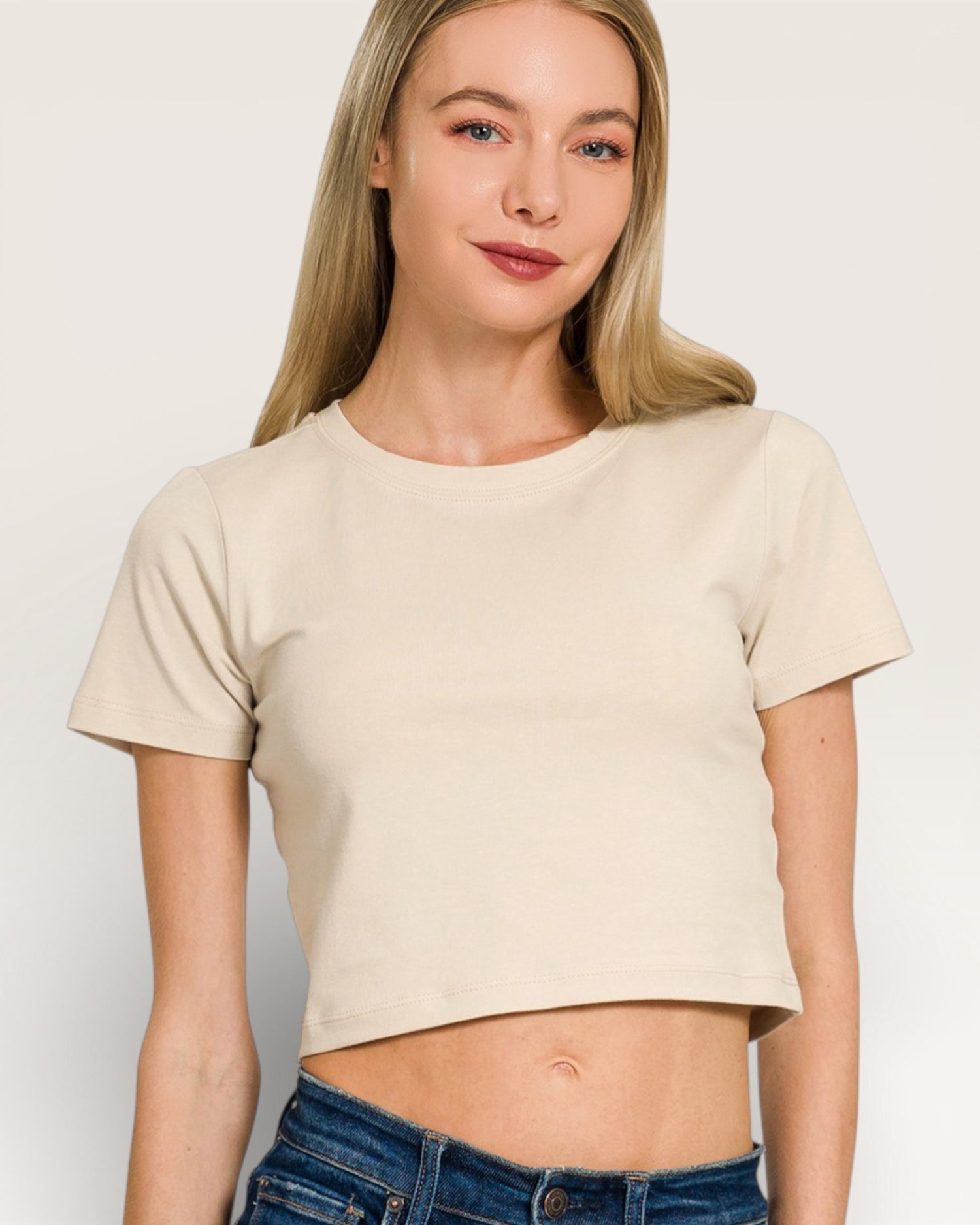 Woman wearing a beige crop top and blue jeans on a plain background