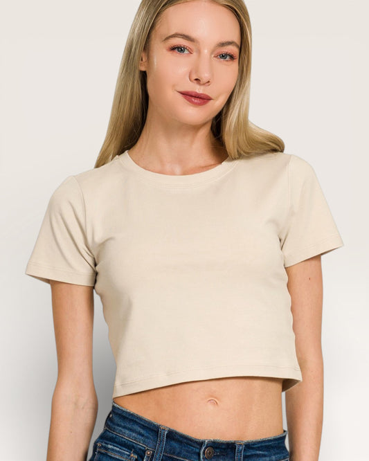 Woman wearing a beige crop top and blue jeans on a plain background