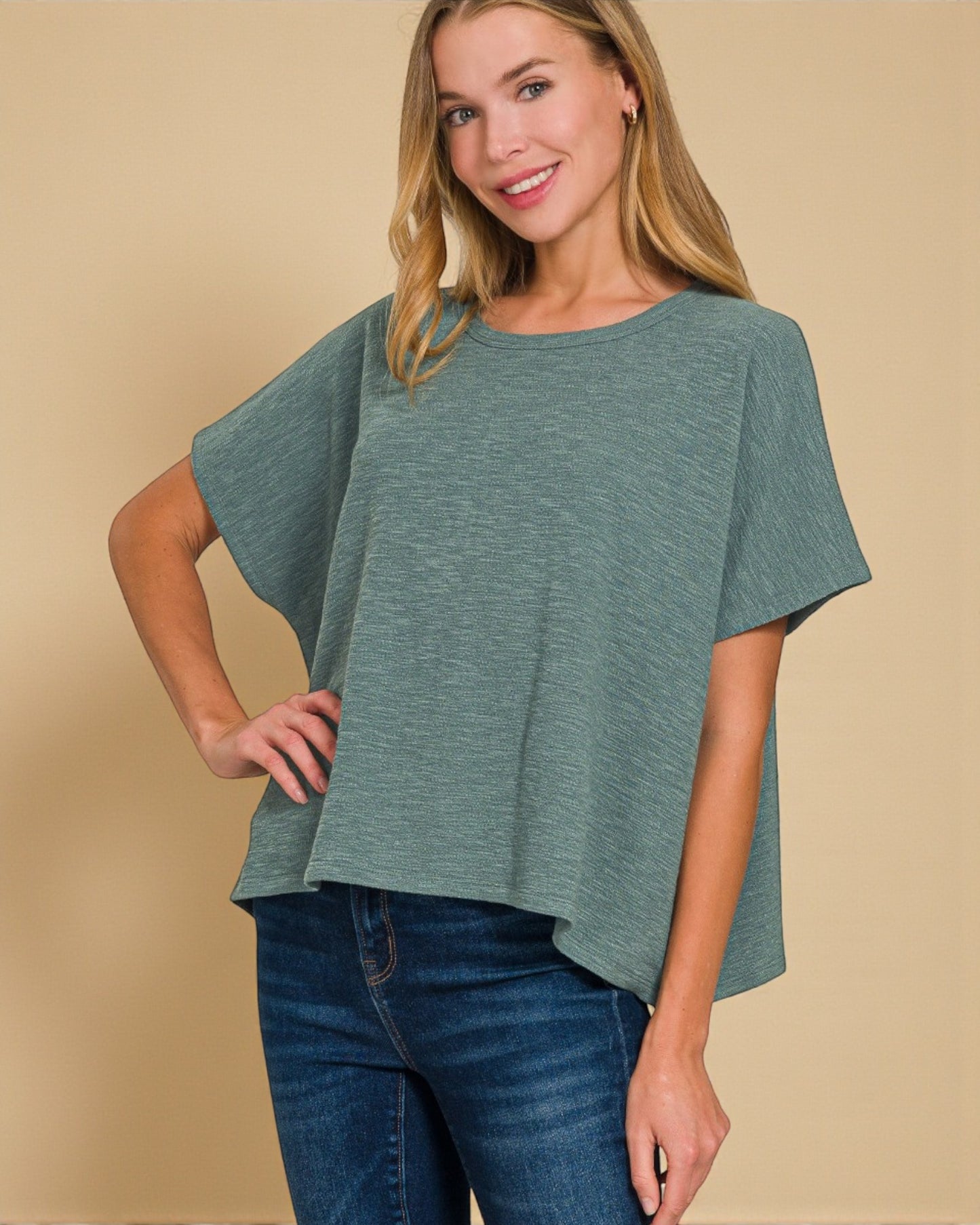 Woman wearing a green oversized top and blue jeans on a beige background