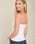 Woman wearing a white strapless top and blue jeans against a beige background