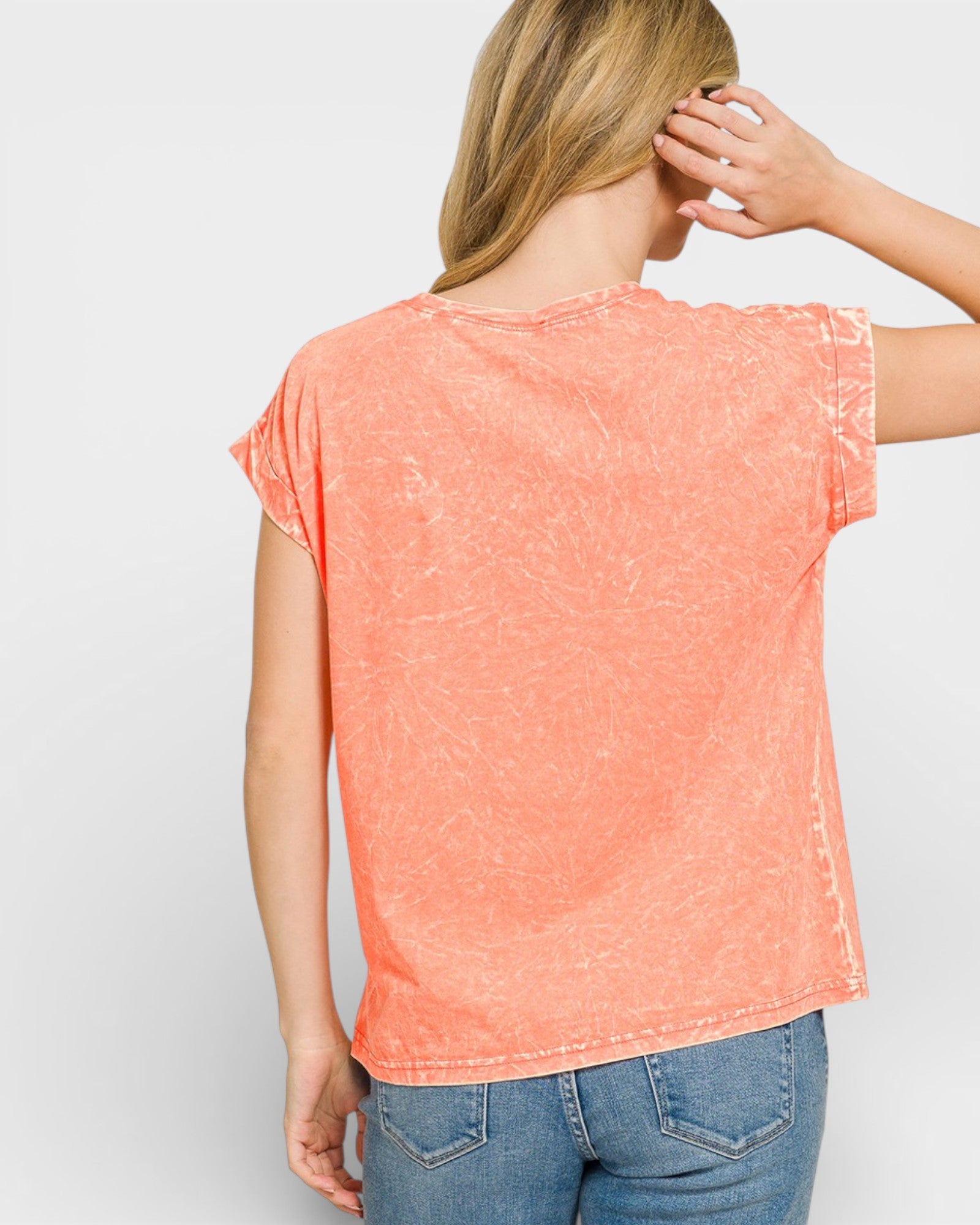 Person wearing a coral t-shirt and blue jeans on a plain background