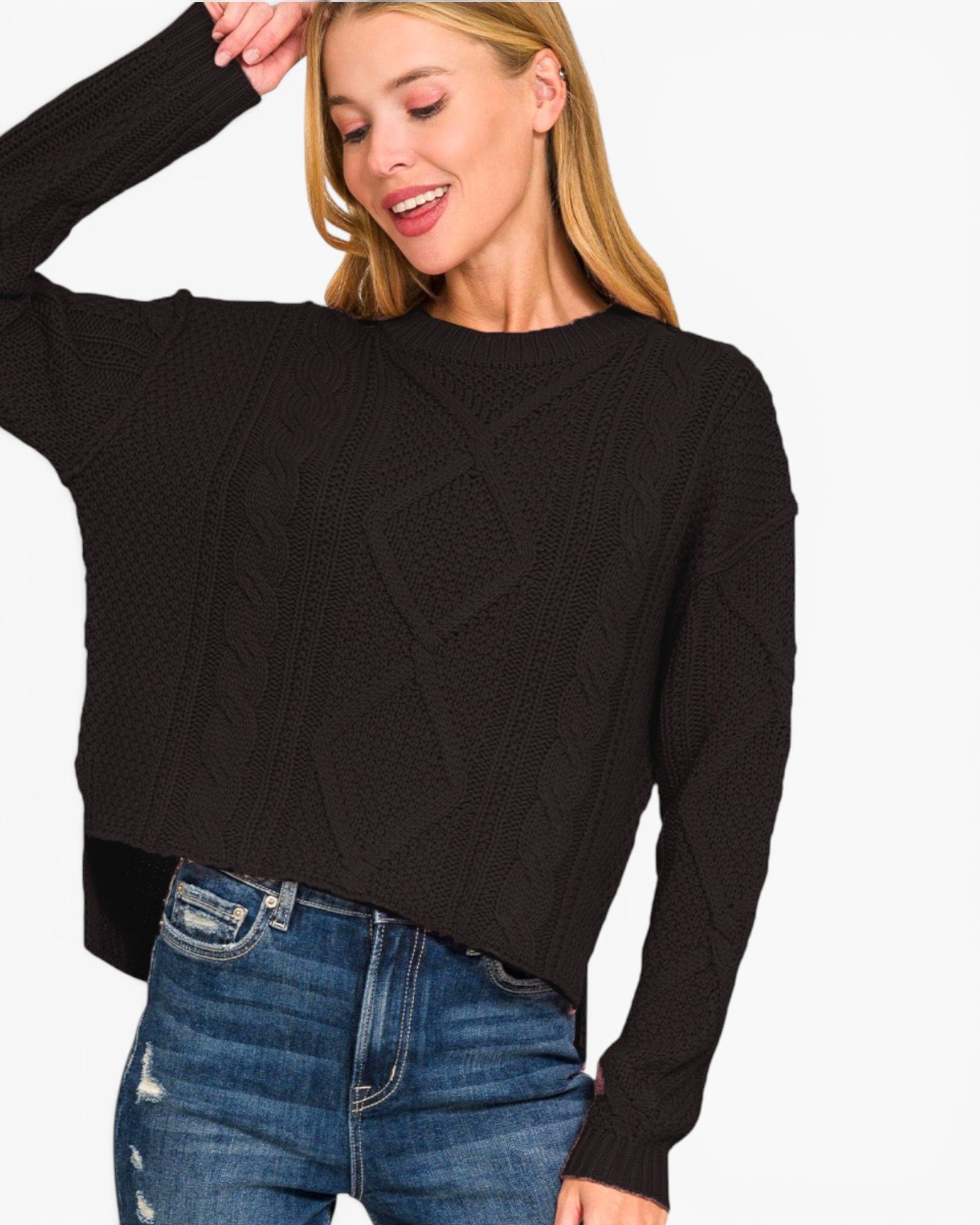 A woman wearing a black long-sleeve cable-knit sweater and blue jeans, cropped from the head down against a plain light background.