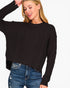 A woman wearing a black long-sleeve cable-knit sweater and blue jeans, cropped from the head down against a plain light background.