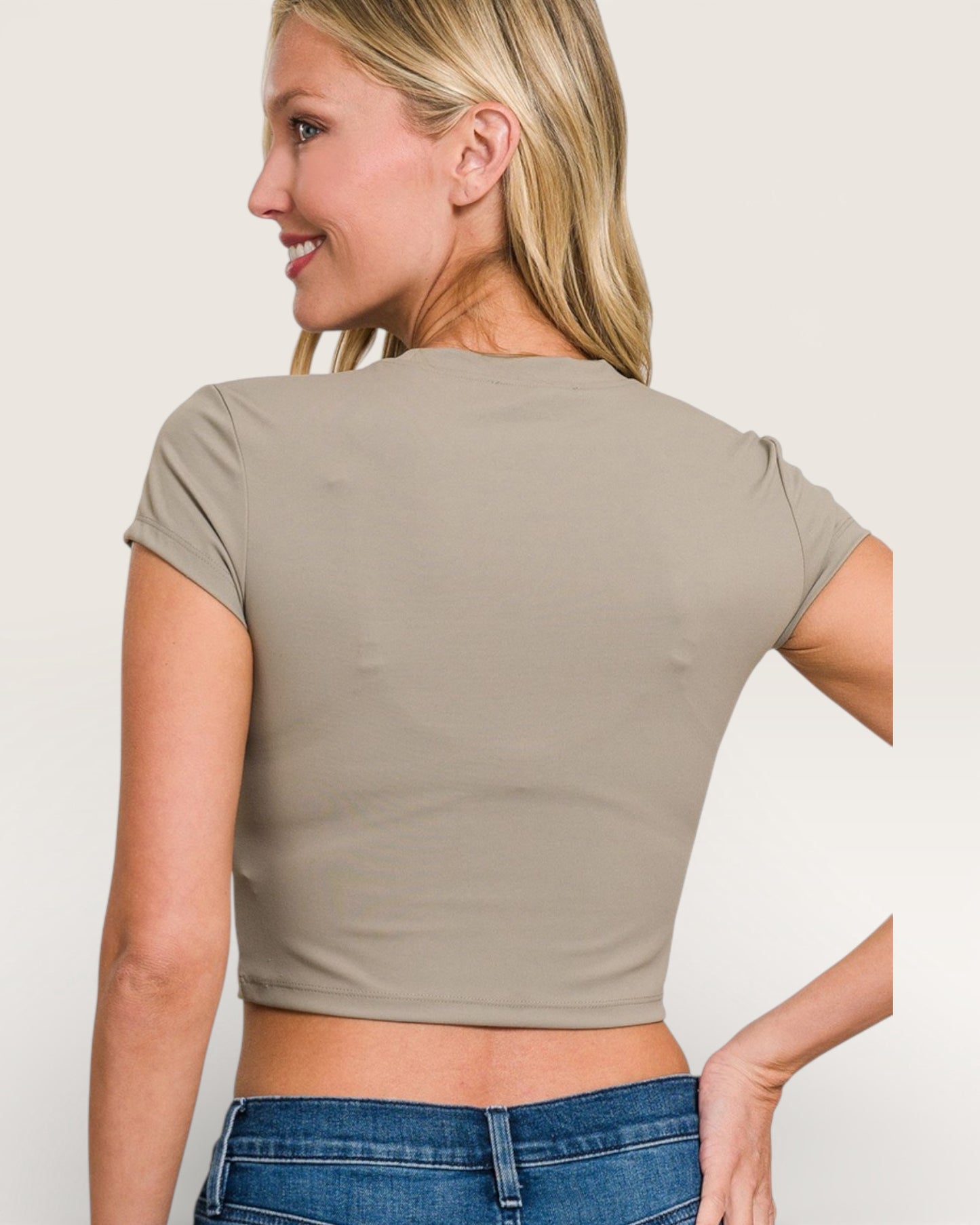 Woman wearing a beige crop top and blue jeans against a plain background