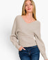 A woman wearing a light beige ribbed knit sweater with a V-neck and long sleeves, paired with blue jeans, photographed against a clean white background.