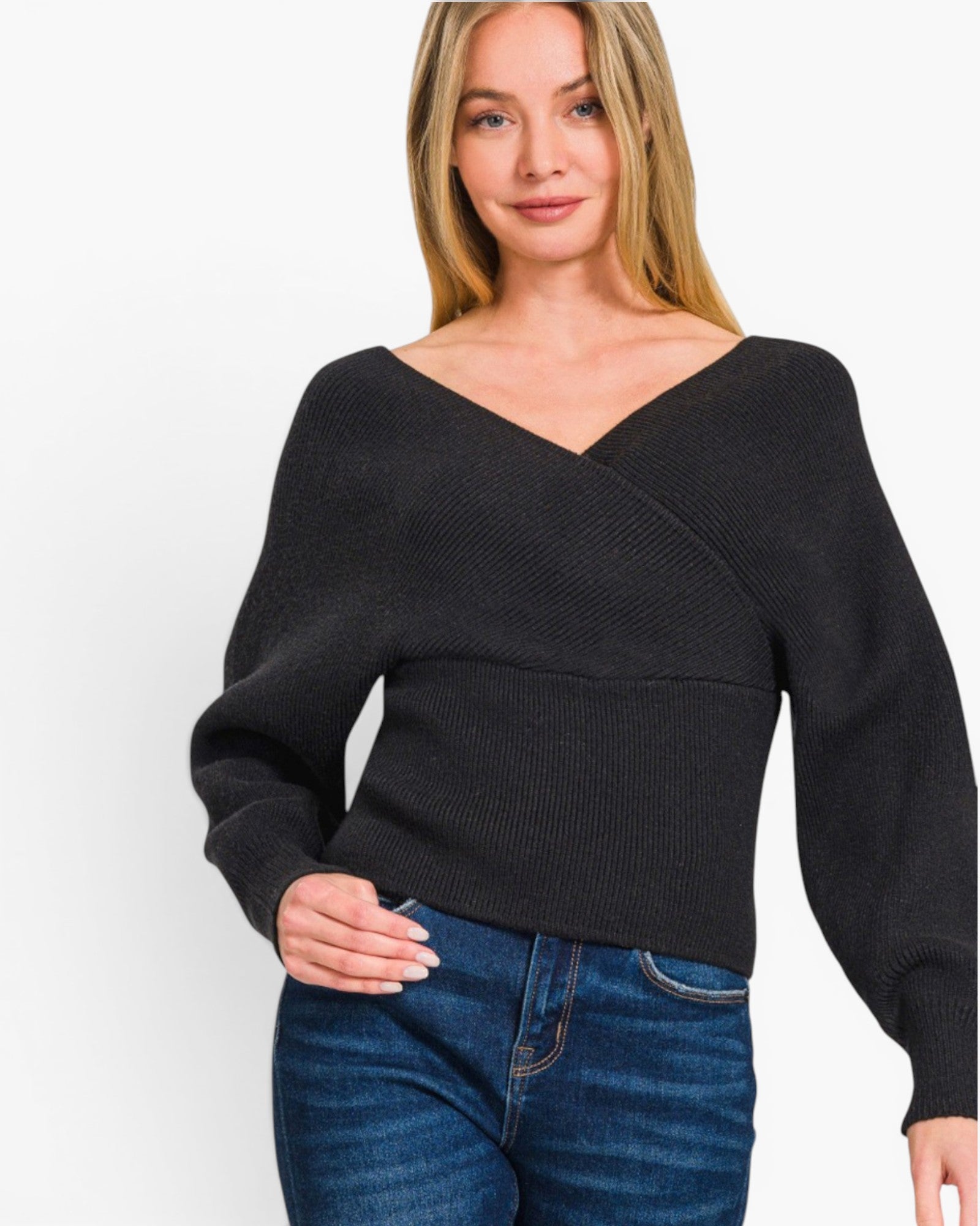 A woman wearing a black long-sleeve knit top with a wide V-neck and wrap-style crossover front, paired with blue jeans, against a plain light background.
