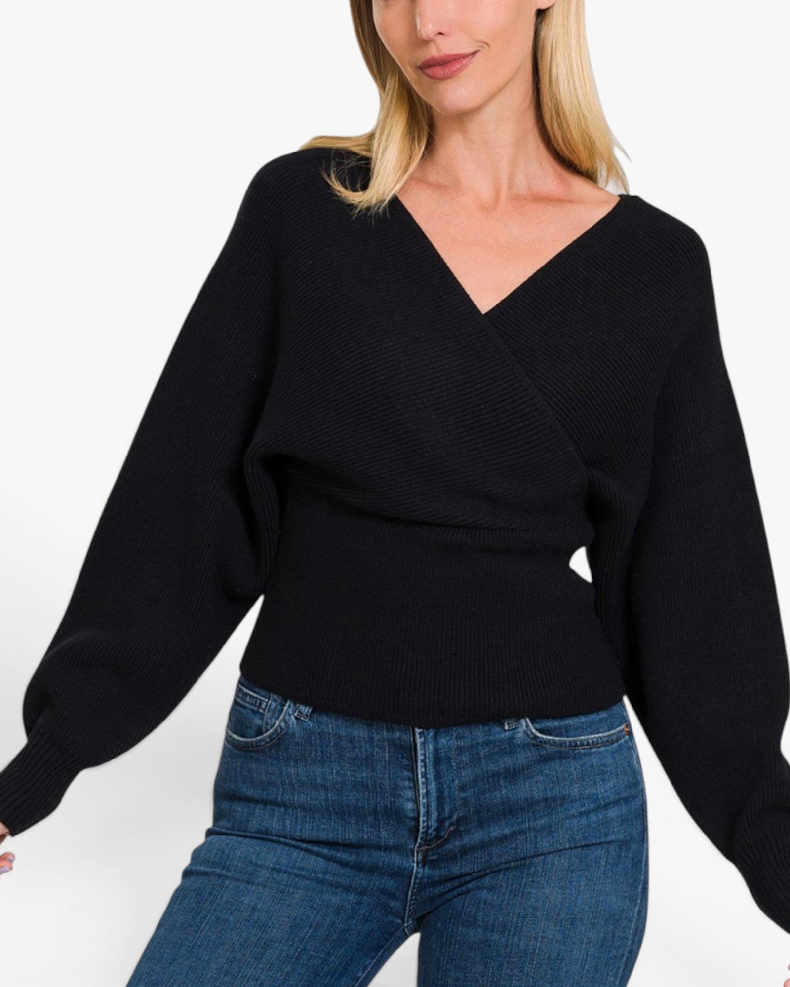 A woman wearing a black knit wrap-style sweater with long balloon sleeves and blue jeans, cropped from the mouth down against a plain white studio background.