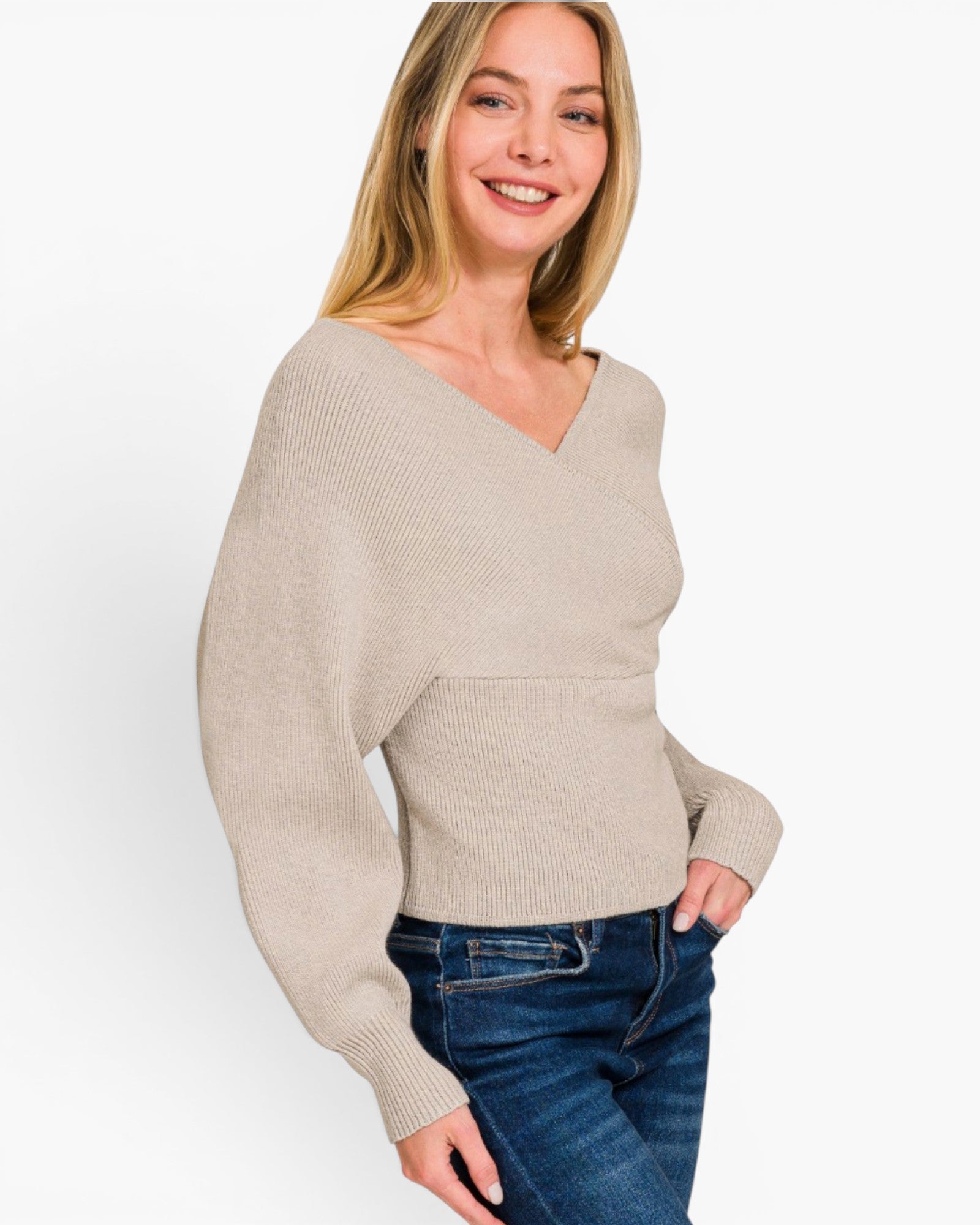 A woman wearing a light beige ribbed knit sweater with a V-neck and long sleeves, paired with blue jeans, photographed against a clean white background.