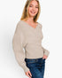 A woman wearing a light beige ribbed knit sweater with a V-neck and long sleeves, paired with blue jeans, photographed against a clean white background.