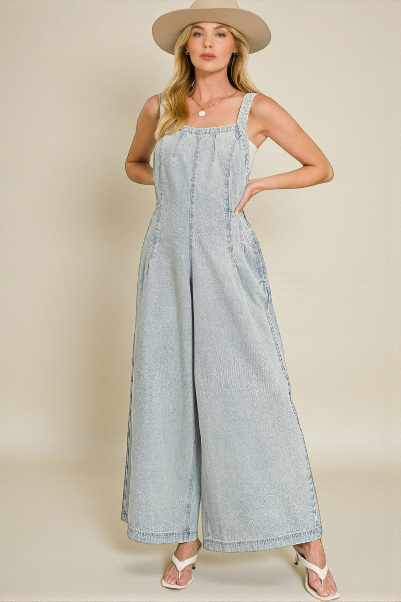 Woman wearing a light blue denim jumpsuit with a beige hat on a beige background