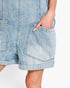 Close-up of a person wearing light-wash denim shorts with large front patch pockets and rolled hems, shown against a plain light background.